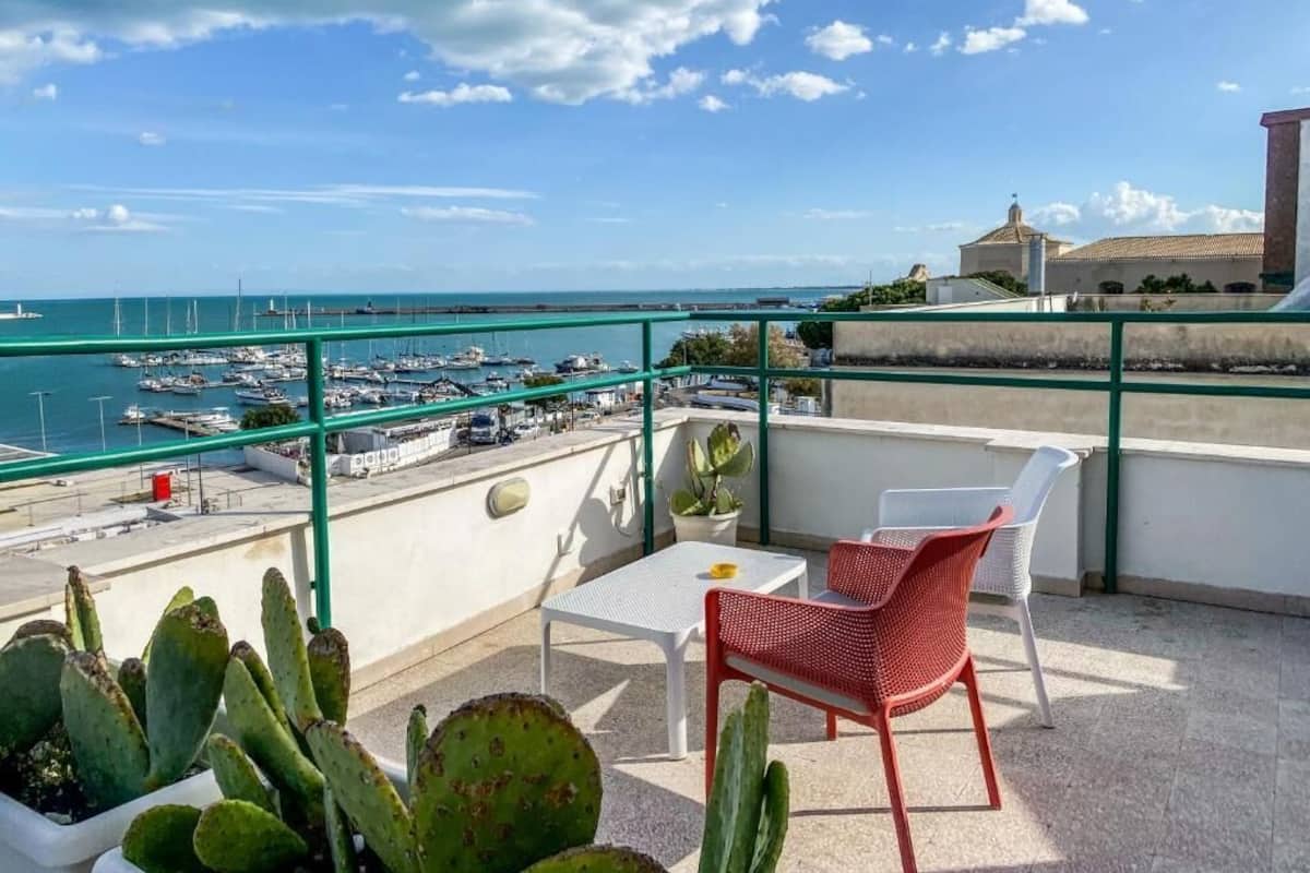 Un balcon avec vue sur la mer, une table, une chaise et des cactus.