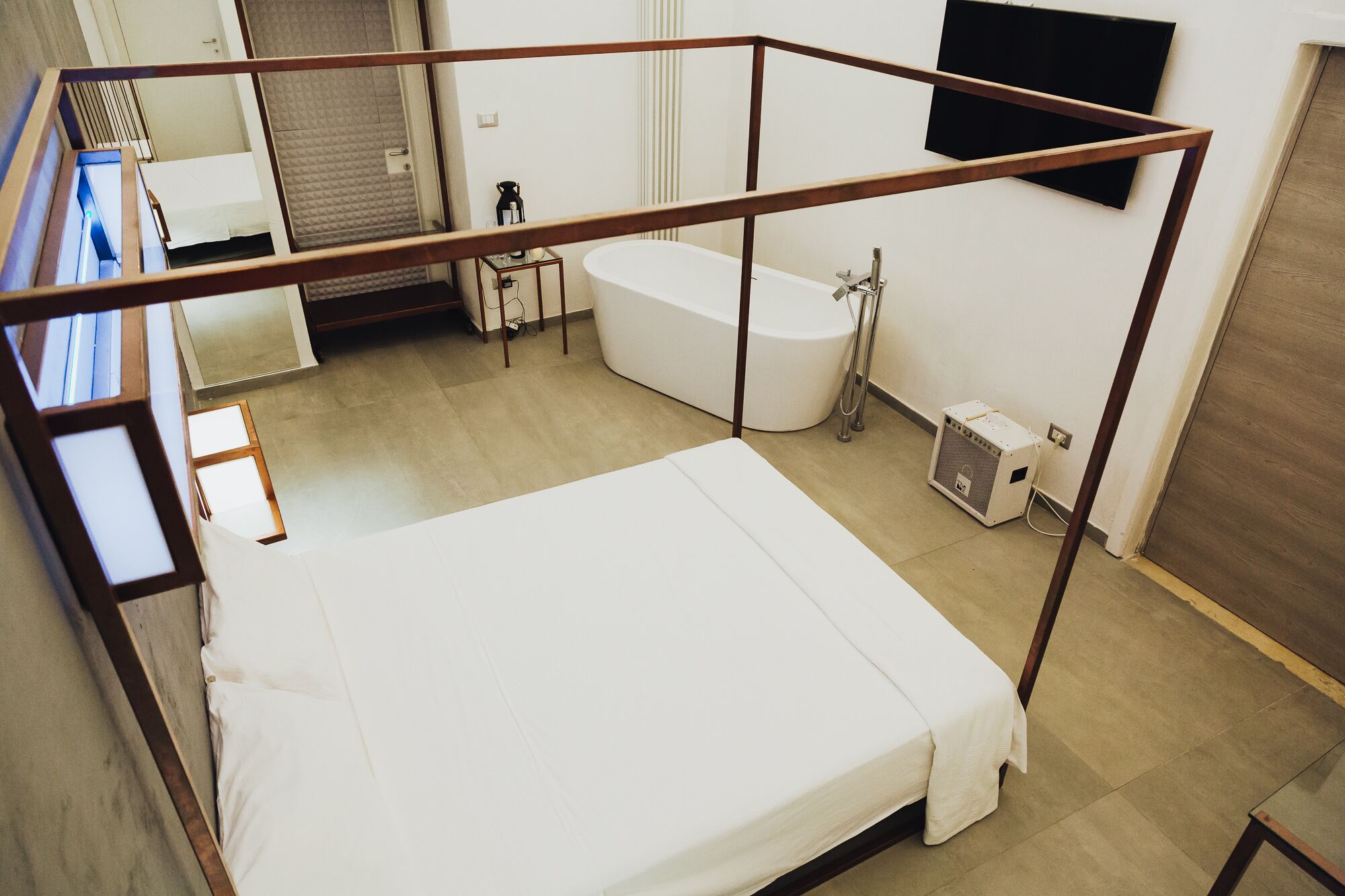 A bedroom with a bed, a window, a bathroom with a bathtub, and a heater.