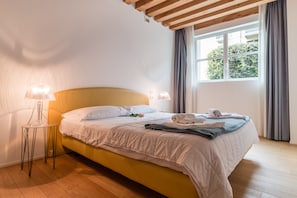 Una cama bien hecha con sábanas blancas, una lámpara de noche y una ventana con cortinas.