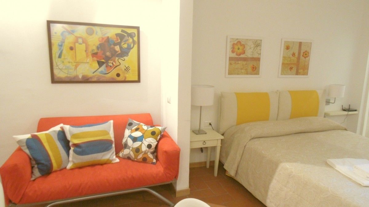 A hotel room with a red sofa, a bed with yellow and white bedding, and two wall-mounted lamps.