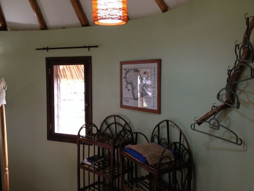 A room with a wooden ceiling, a window with a view, a framed map on the wall, and a metal rack with items.