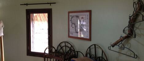 A room with a wooden ceiling, a window with a view, a framed map on the wall, and a metal rack with items.