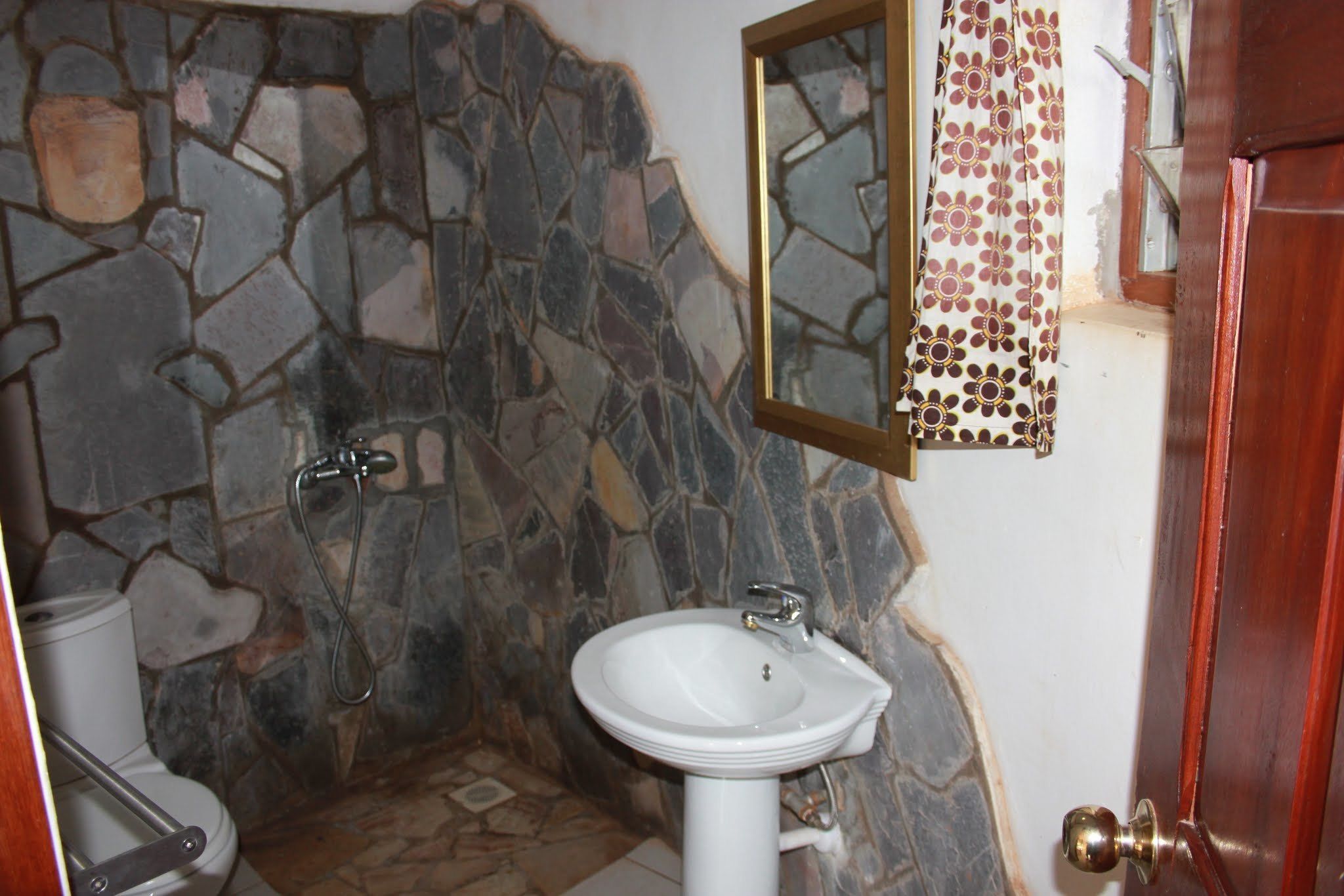 Une salle de bain avec un mur en pierre, un lavabo blanc et une douche.
