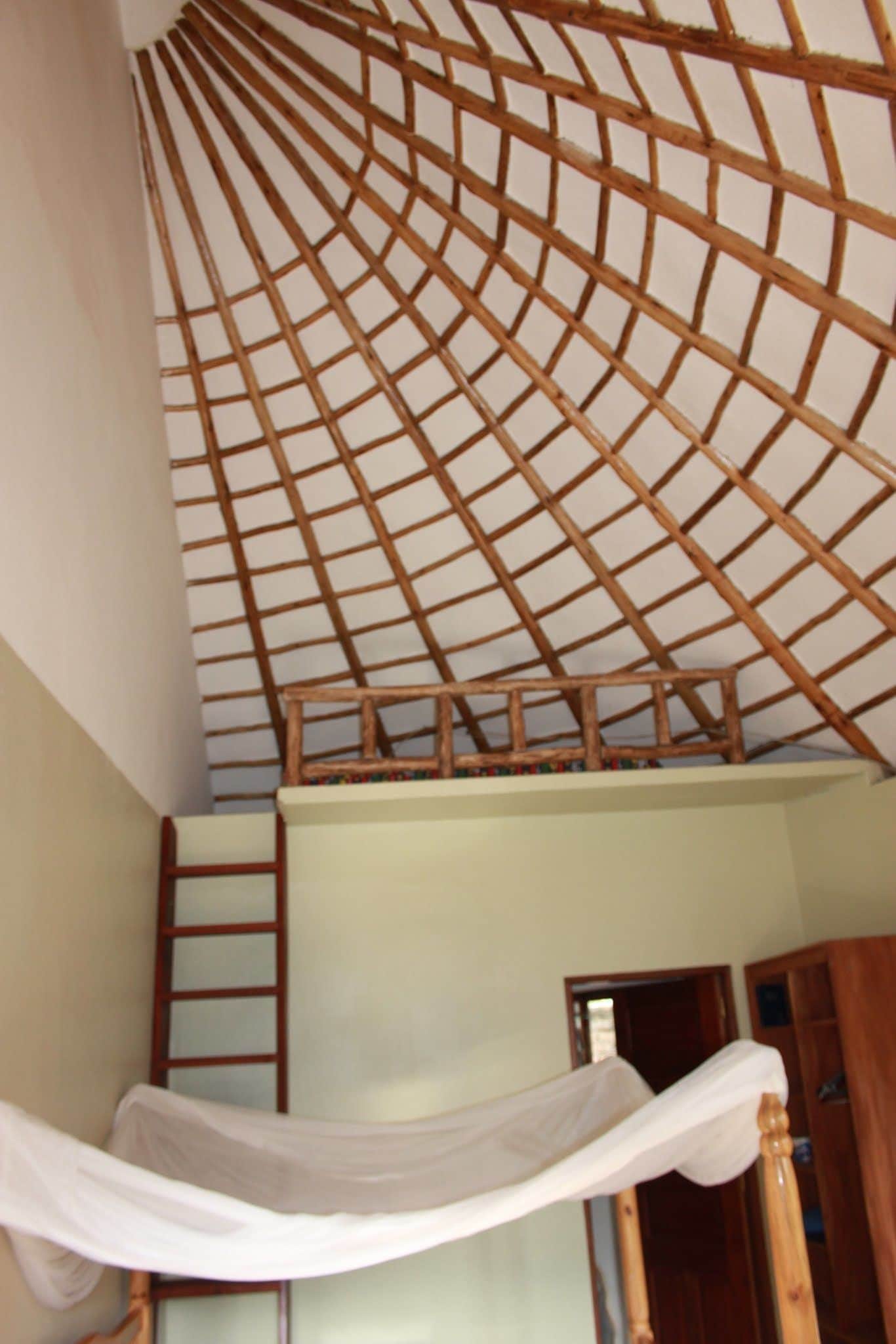 Une pièce avec un plafond en pente, une échelle en bois et un lit à baldaquin blanc.