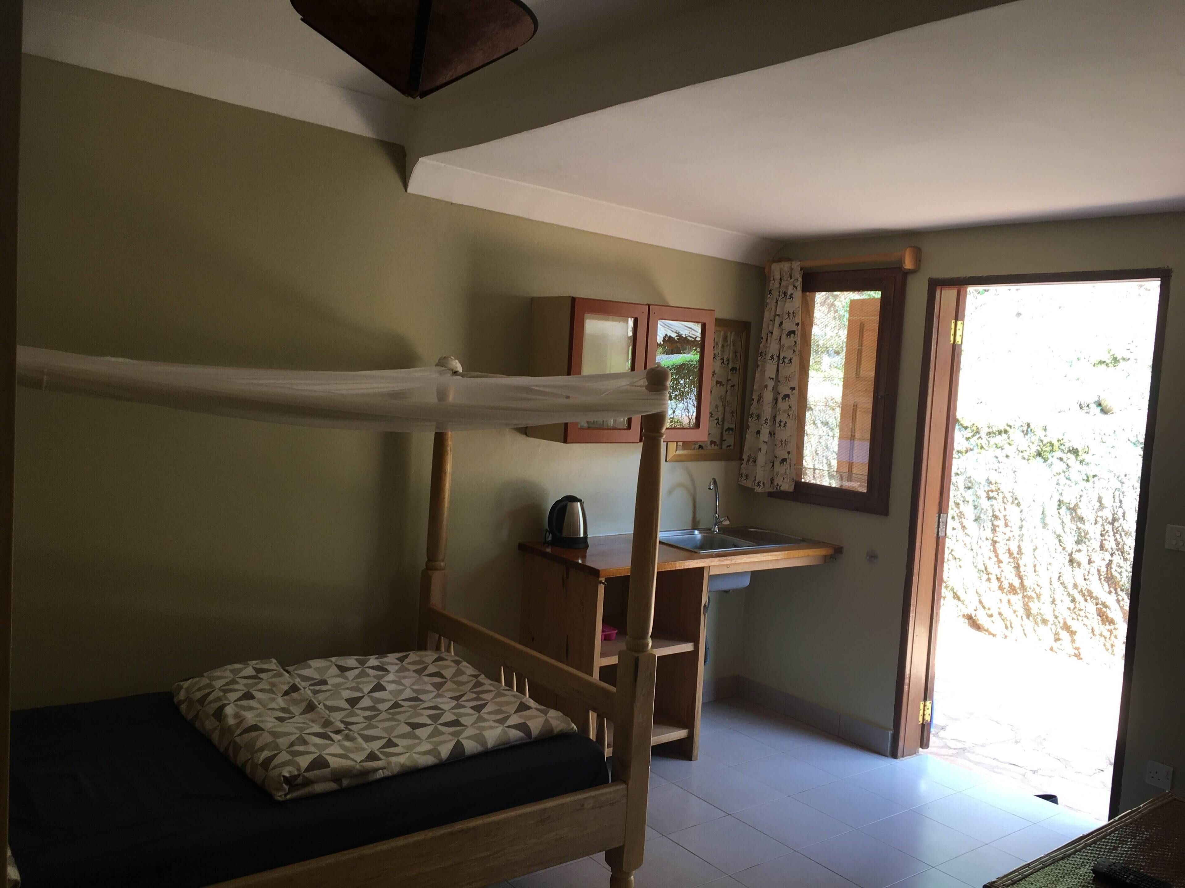 A room with a bunk bed, a small wooden desk with a sink, and a window with curtains.
