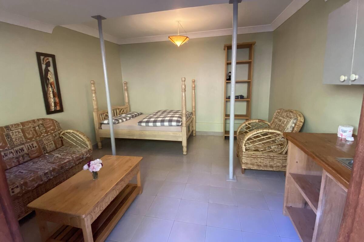 Una habitación acogedora con una cama, un sofá, una mesa de madera y un sillón de mimbre.