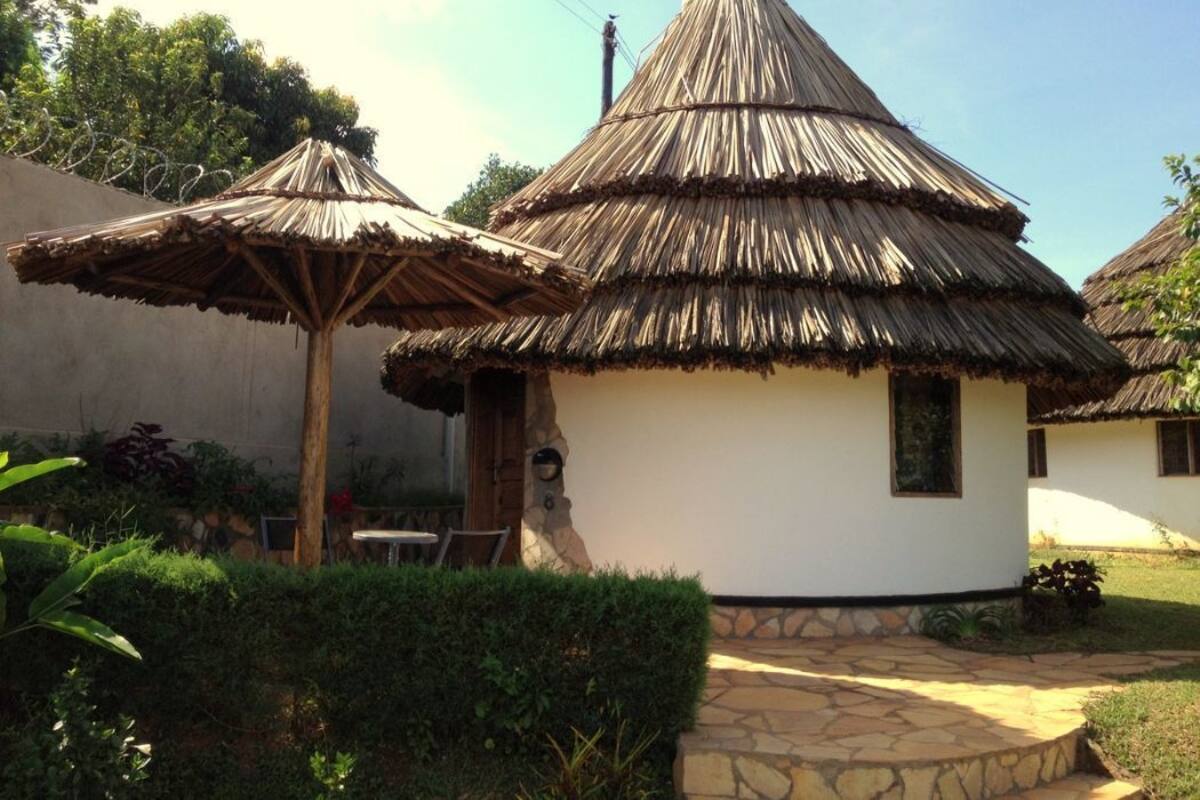 Una cabaña tradicional con techo de paja, con un sendero de piedra que la lleva al frente, rodeada de follaje.