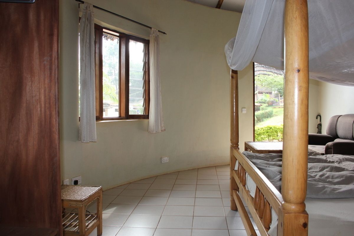Un dormitorio con estructura de cama de madera, una mesita pequeña y una ventana con cortinas.
