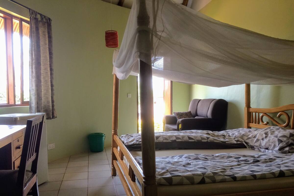 Un dormitorio con una cama litera, un escritorio, una silla, un cubo de basura verde y un sofá.