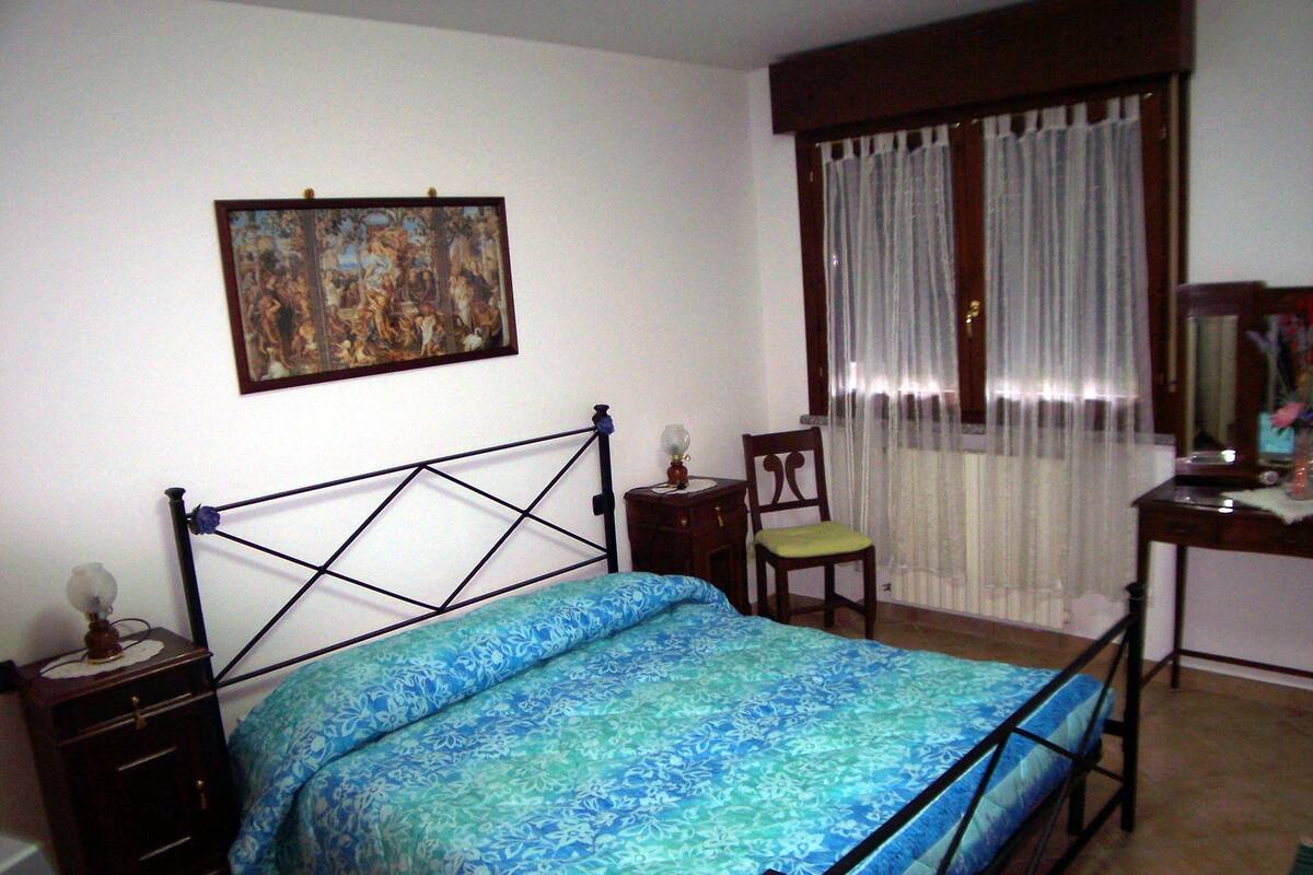 Um quarto com uma cama, uma cadeira, uma escrivaninha e um quadro na parede.