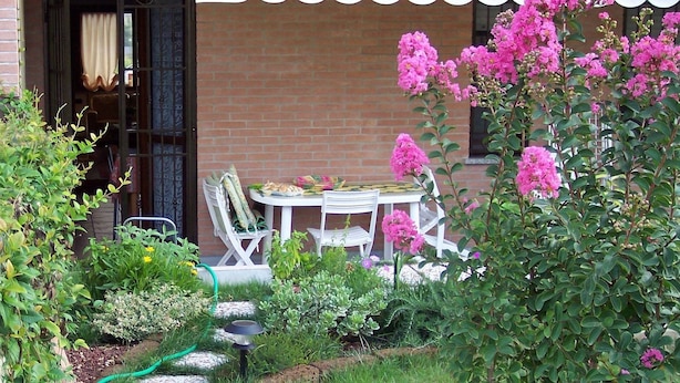 A garden with a table and chairs, a brick wall, and a white awning. - B&B Il Parco (Parma)