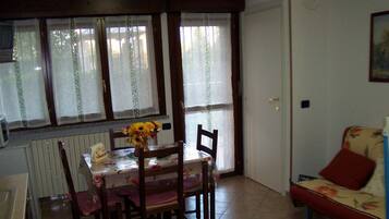 Zona pranzo con tavolo e sedie, un termosifone, una finestra con tende e un divano.