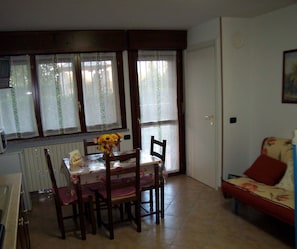 Un coin repas comprenant une table et des chaises, un radiateur, une fenêtre avec des rideaux et un canapé.