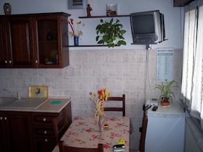 Une cuisine avec des meubles de rangement en bois, un pare-feu en carreaux, une petite télévision et un calendrier accroché au mur.
