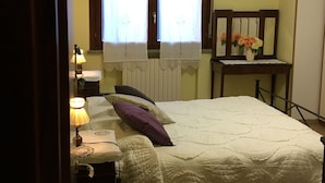 A bedroom with a bed, a nightstand, a lamp, a dresser, a mirror, and a window with curtains. - B&B Il Parco (Parma)