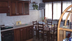 A kitchen with wooden cabinets, a built-in oven, a dining table with chairs, a television, and a window with curtains. - B&B Il Parco (Parma)