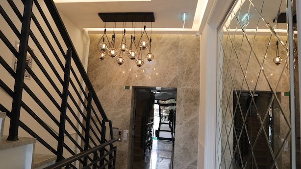 Un interior moderno con suelo de mármol, una escalera con barandilla negra y un separador de vidrio con diseño geométrico.