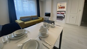 Habitación de hotel moderna con comedor listo para una comida, un sofá, un televisor y una cama con un cuadro.