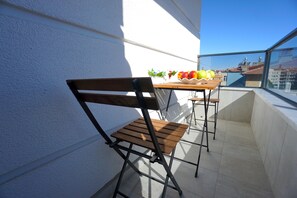 A balcony with a wooden chair and table, a white wall, and a view of buildings.