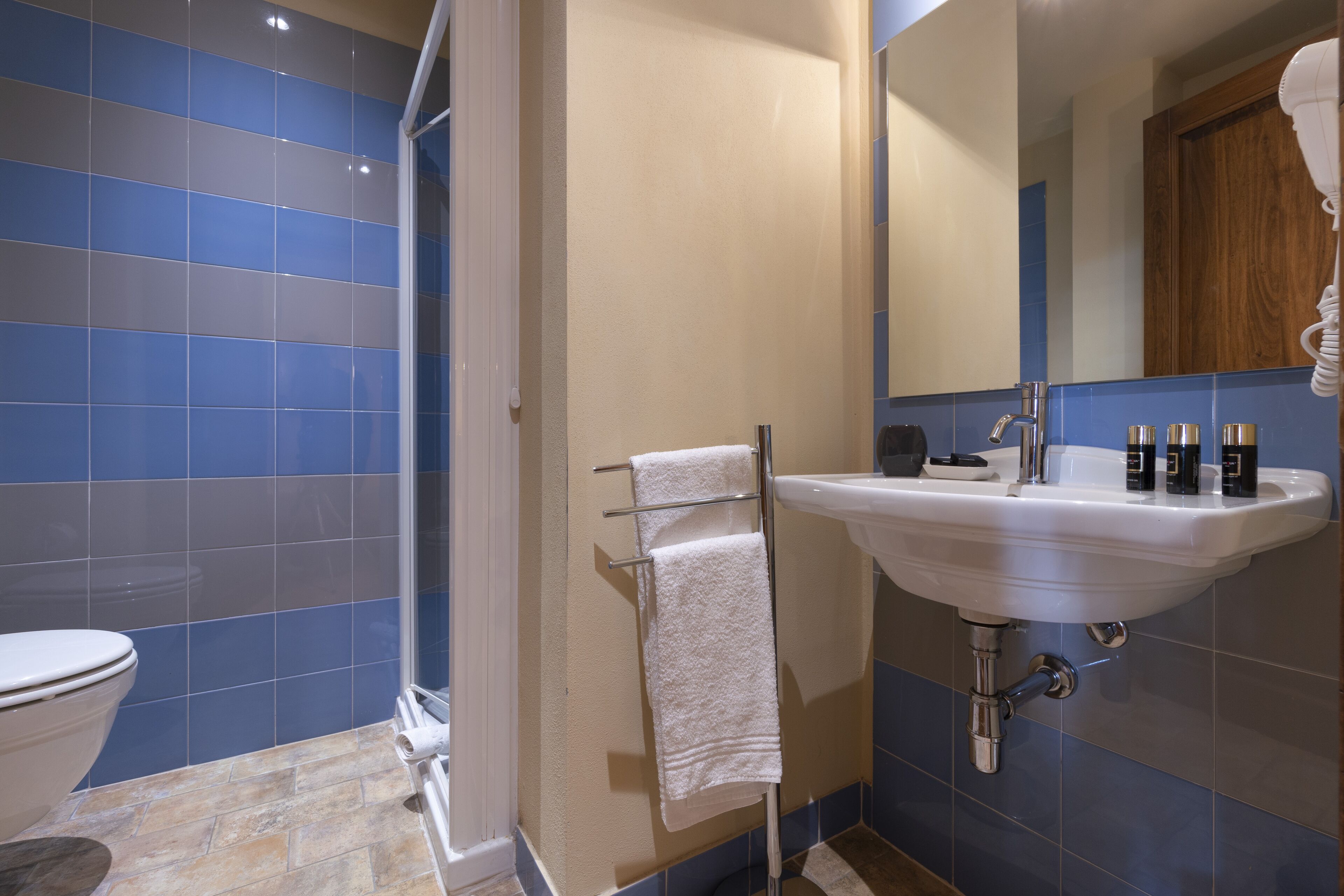 Ein Badezimmer mit einem weißen Waschbecken, blauen Fliesen, einer Duschkabine aus Glas und einem Holzschrank.