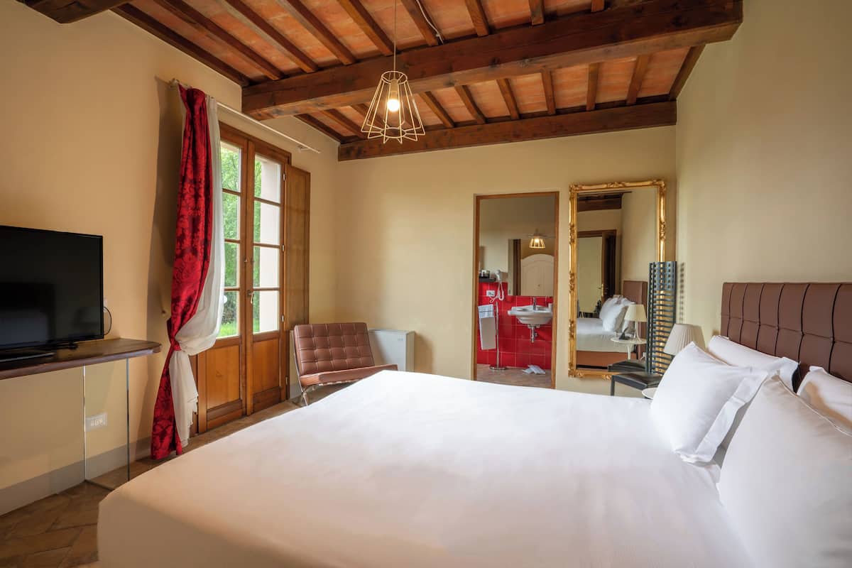 Une chambre d’hôtel équipée d’un lit, d’une télévision, d’une chaise, d’un bureau, d’un miroir et d’une fenêtre avec des rideaux.