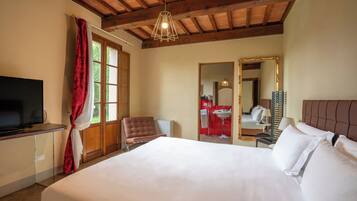 Habitación de hotel con cama, televisión, una silla, escritorio, espejo y ventana con cortinas.