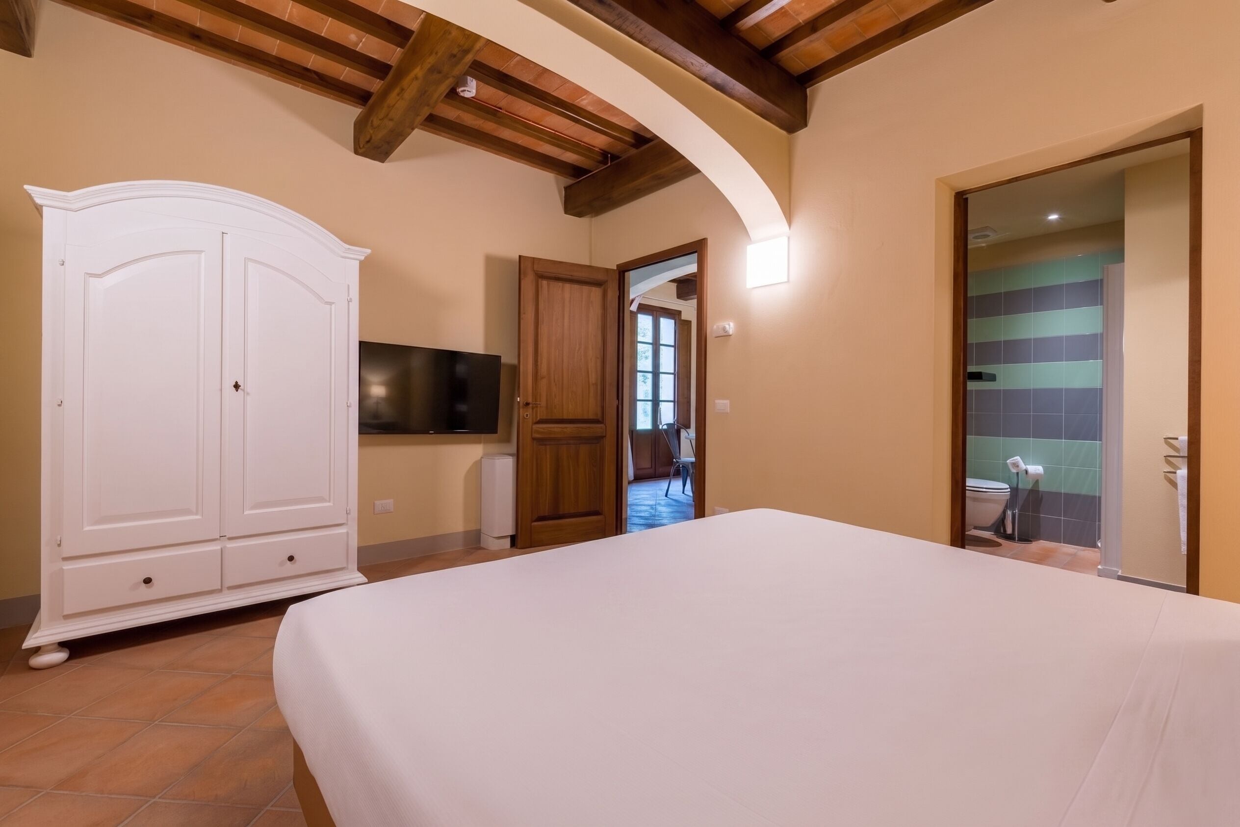 A bedroom with a large bed, a wardrobe, a television, and a bathroom visible through an open door.