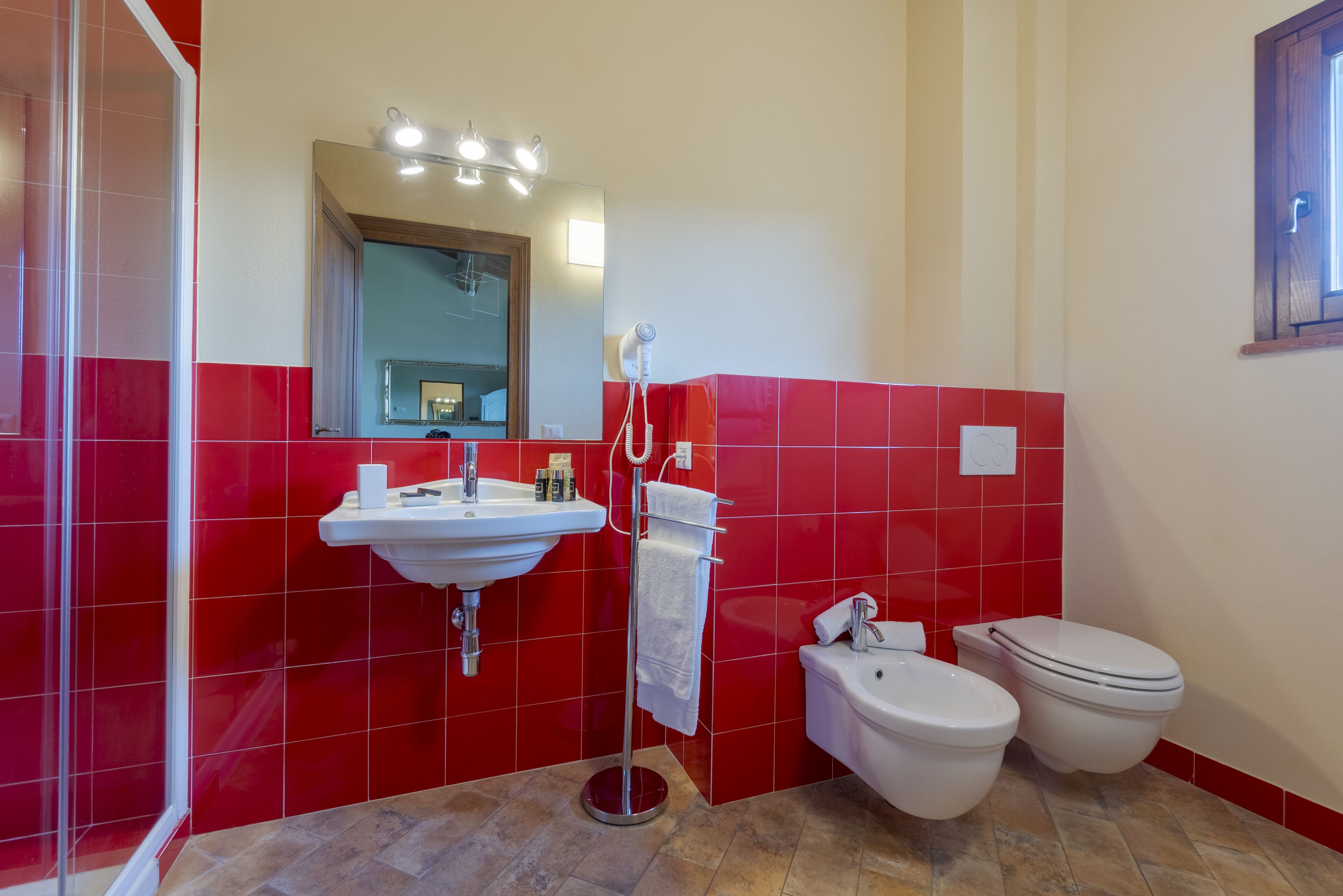 A bathroom with red tiles, a sink, a mirror, a towel rack, and two toilets.
