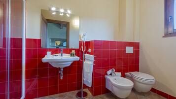 A bathroom with red tiles, a sink, a mirror, a towel rack, and two toilets.