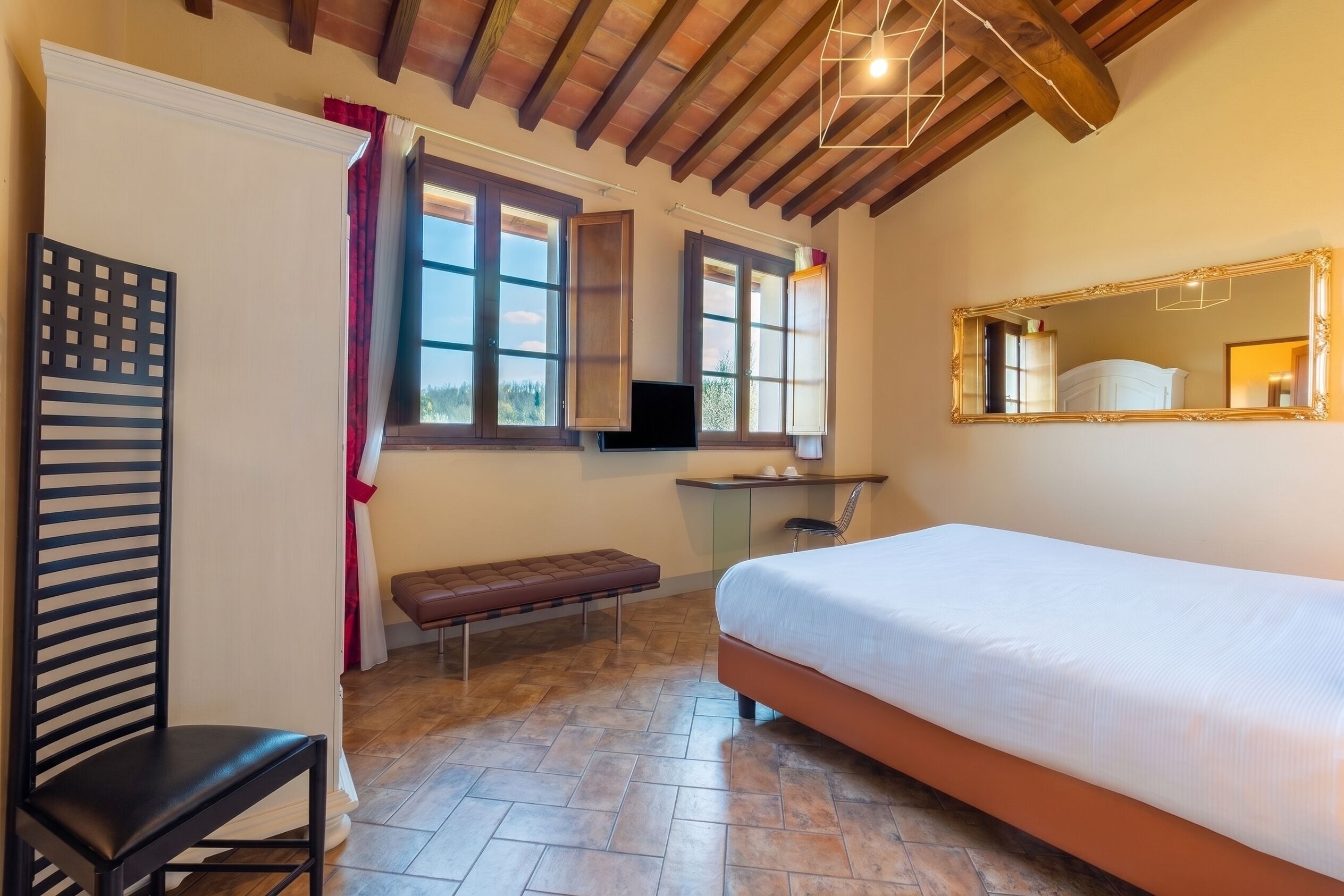 Ein Schlafzimmer mit einem Bett, einem Schreibtisch, einem Stuhl, einer Bank und einem großen Spiegel.