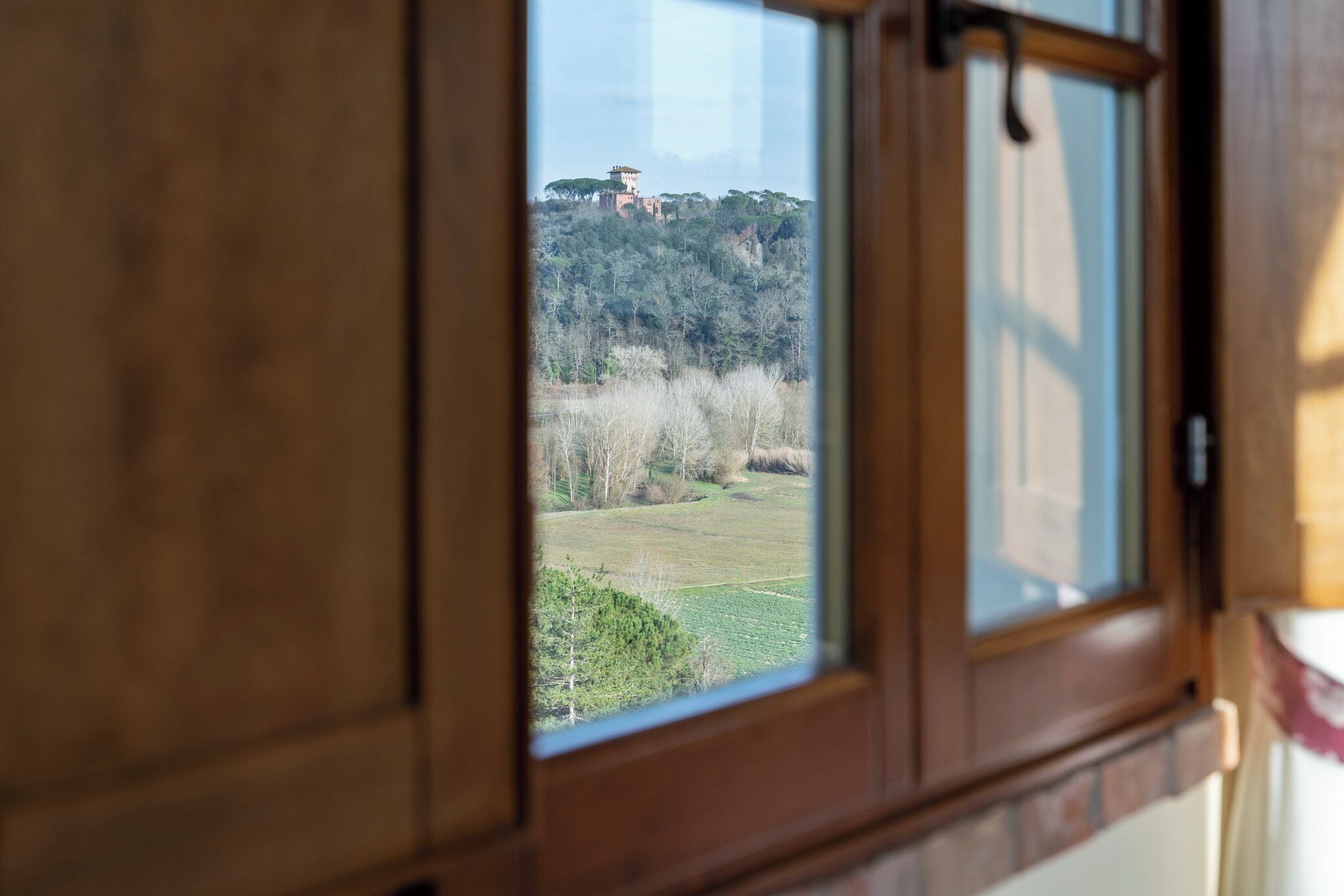 A window with a view of a building on a hill and a field.