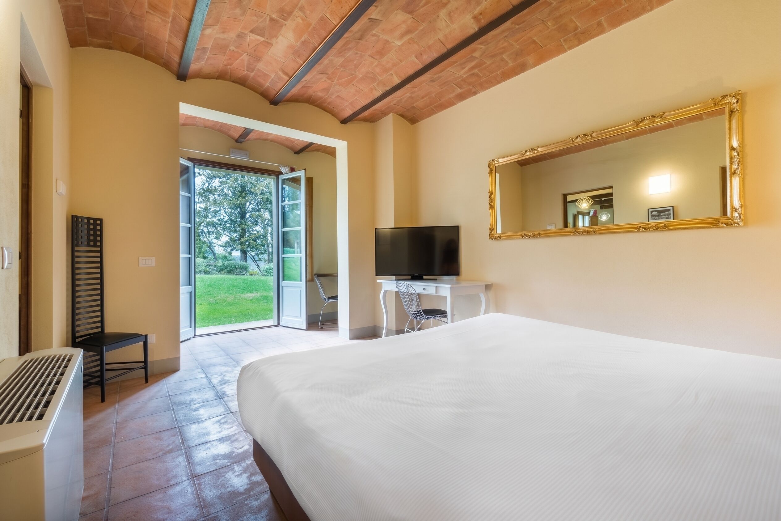 Habitación de hotel con una cama grande, televisor, espejo y vista al exterior.