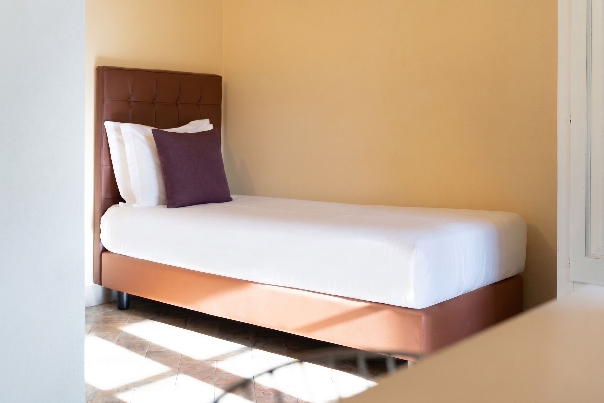 Una cama individual con cabecera, ropa de cama blanca y dos almohadas.
