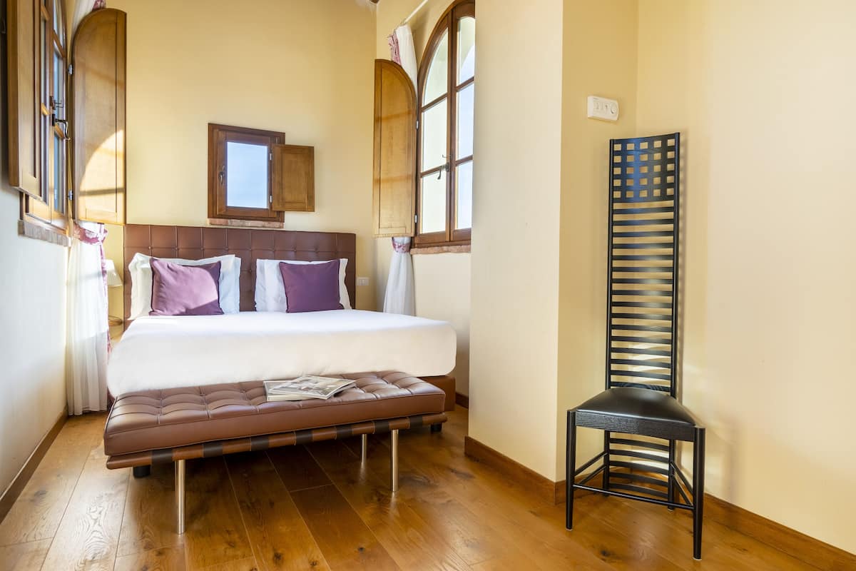 Une chambre à coucher avec un lit, un plancher en bois, une fenêtre et une chaise.