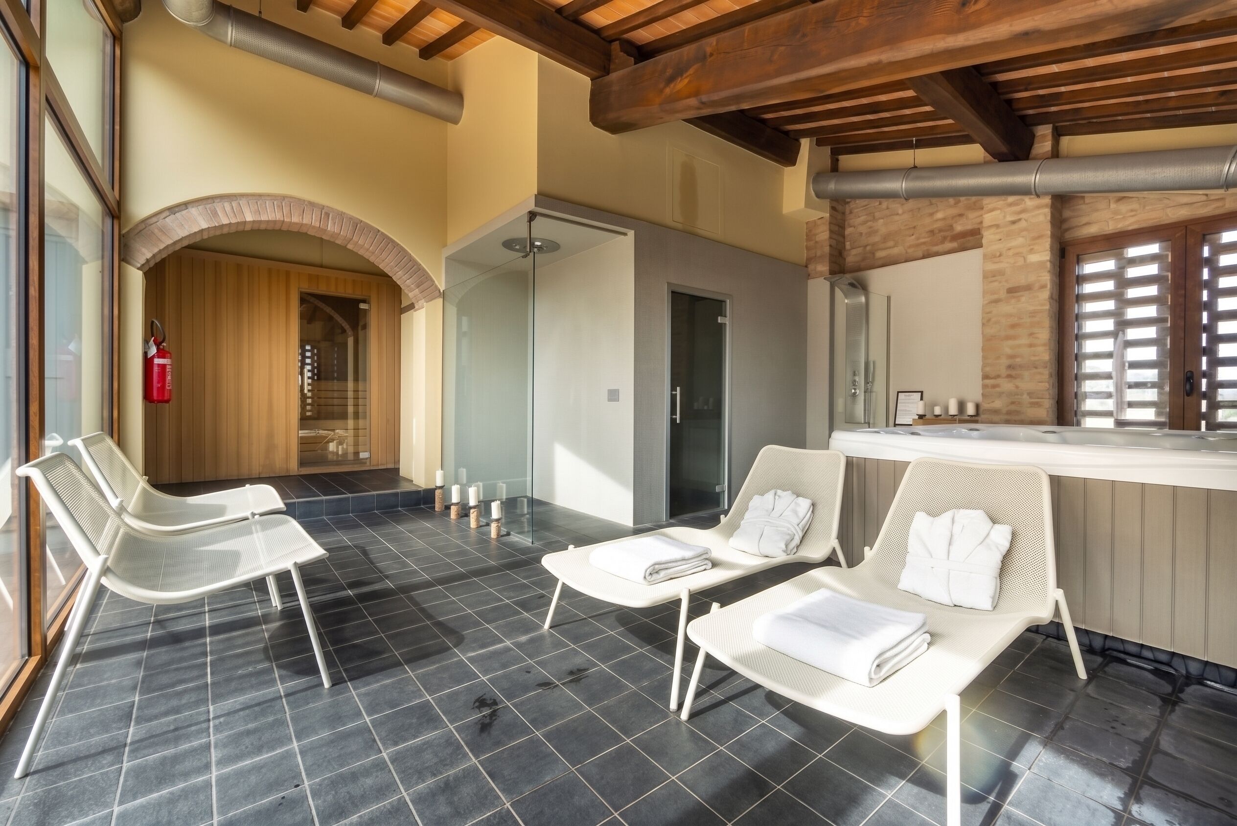 A spa area with two white lounge chairs, a glass-enclosed shower, and a wooden ceiling.
