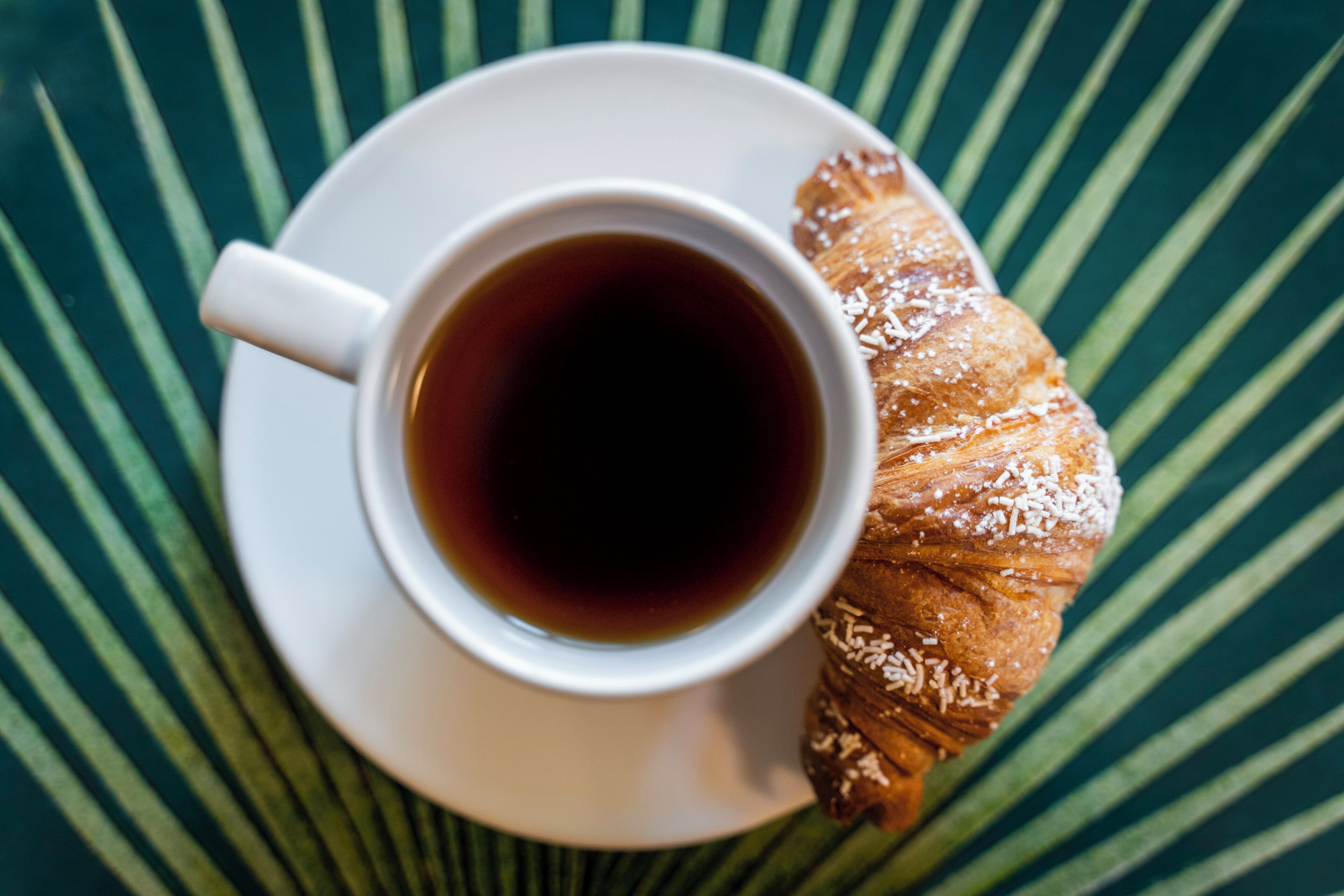 Eine Tasse Kaffee auf einem Untertasse mit einem Gebäck auf einer grün gestreiften Tischdecke.