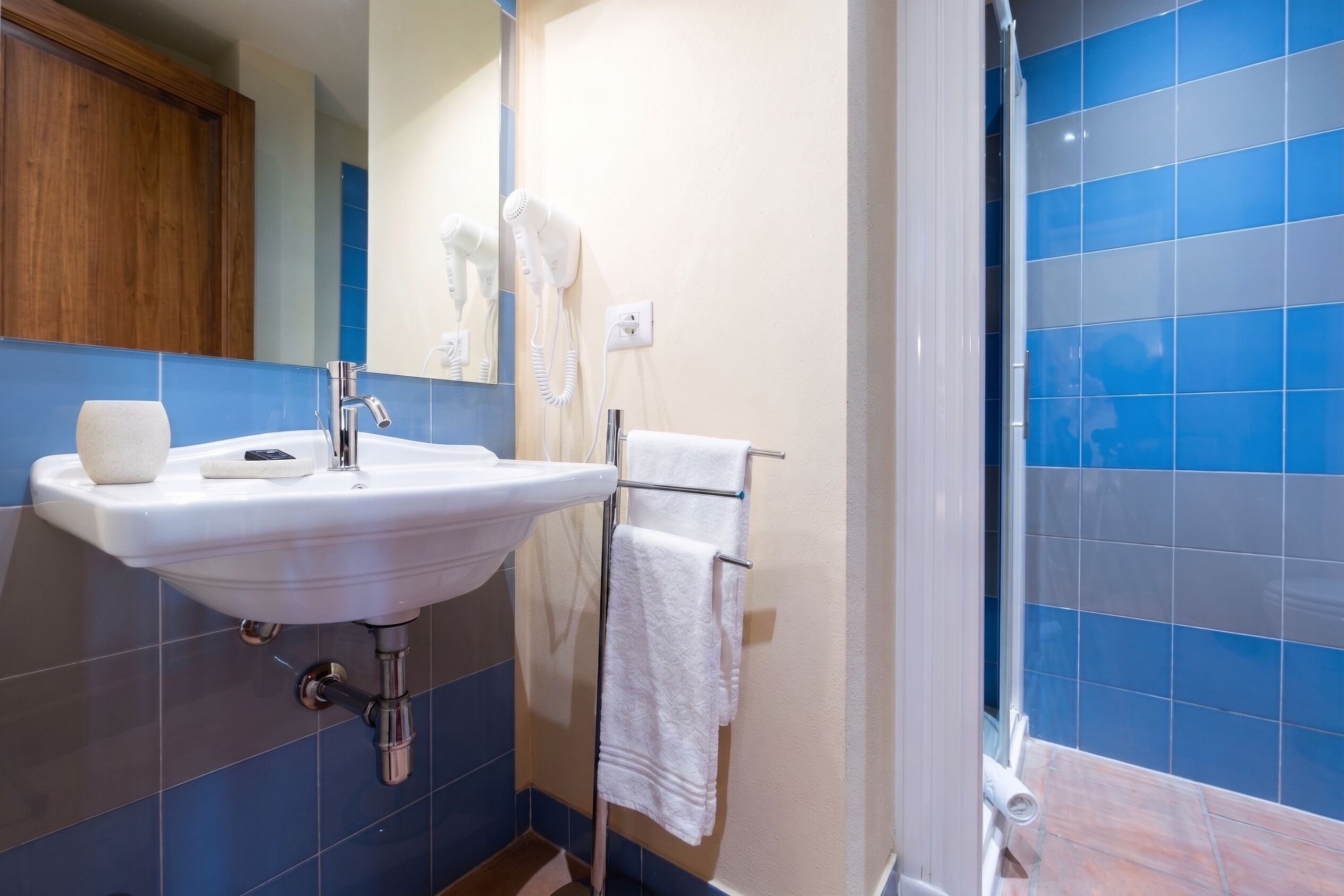 Un baño con un lavabo blanco, un espejo, un perchero para toallas y baldosas azules.