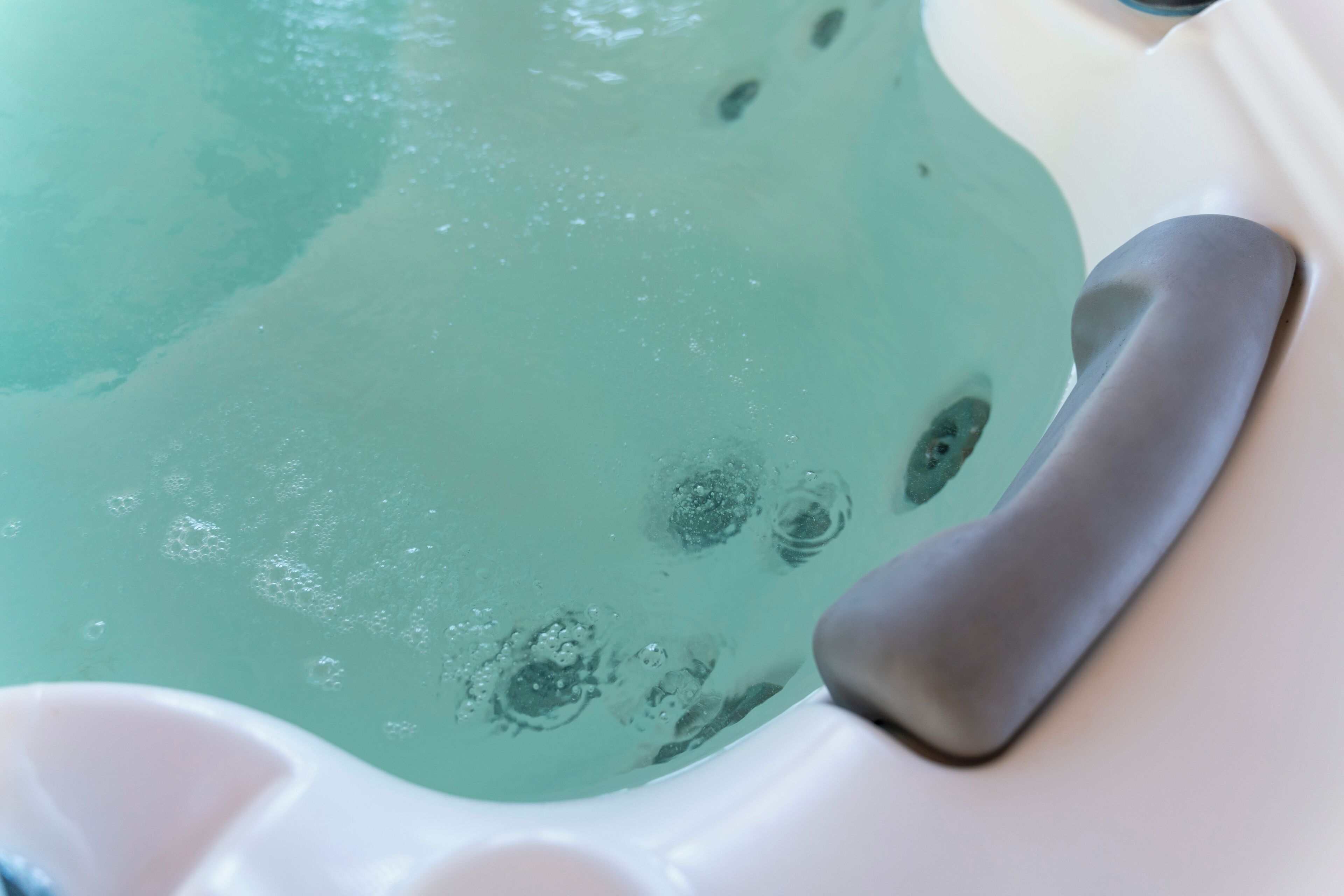 A close-up of a bathtub with a clear blue water feature and a gray bath mat.
