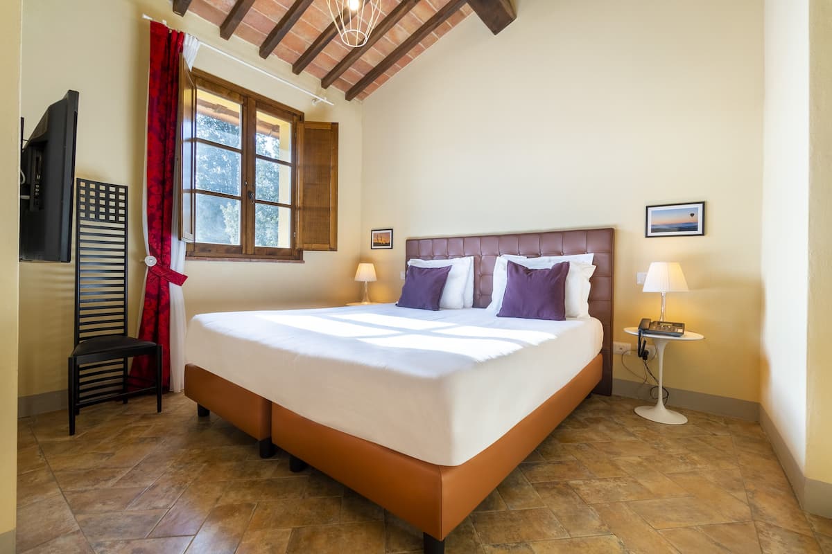 Une chambre spacieuse avec un grand lit, un téléviseur fixé au mur et une fenêtre ornée de rideaux rouges.