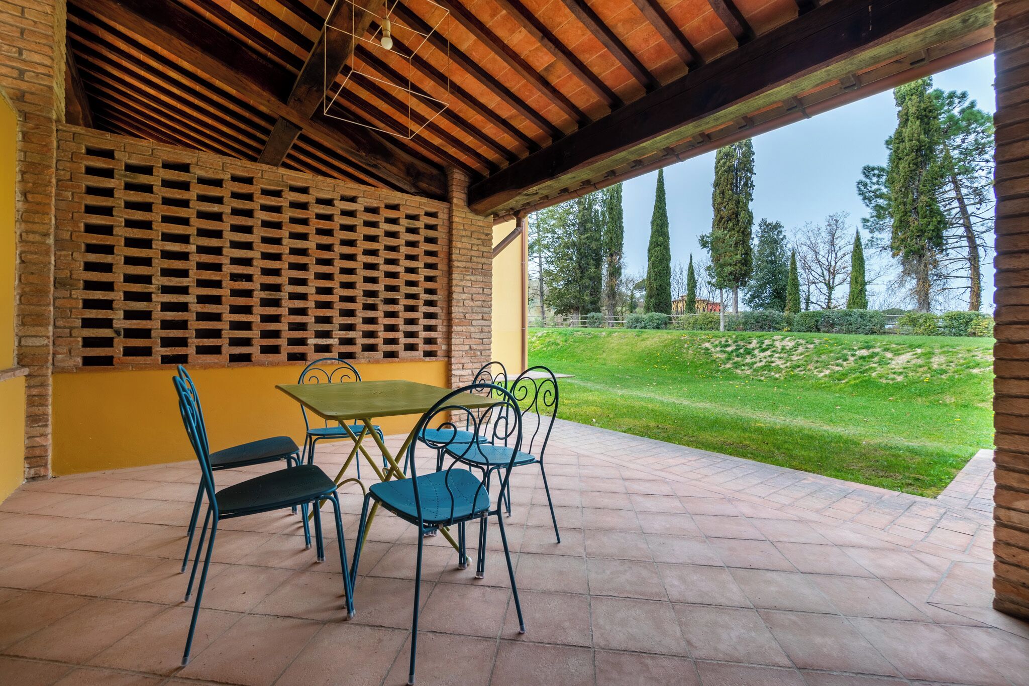 Une terrasse extérieure avec un mur en briques, une table avec des chaises et une vue sur un espace verdoyant avec des arbres.