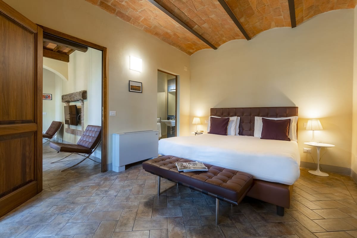 Une chambre à coucher avec un grand lit, un banc, une chaise et un miroir.