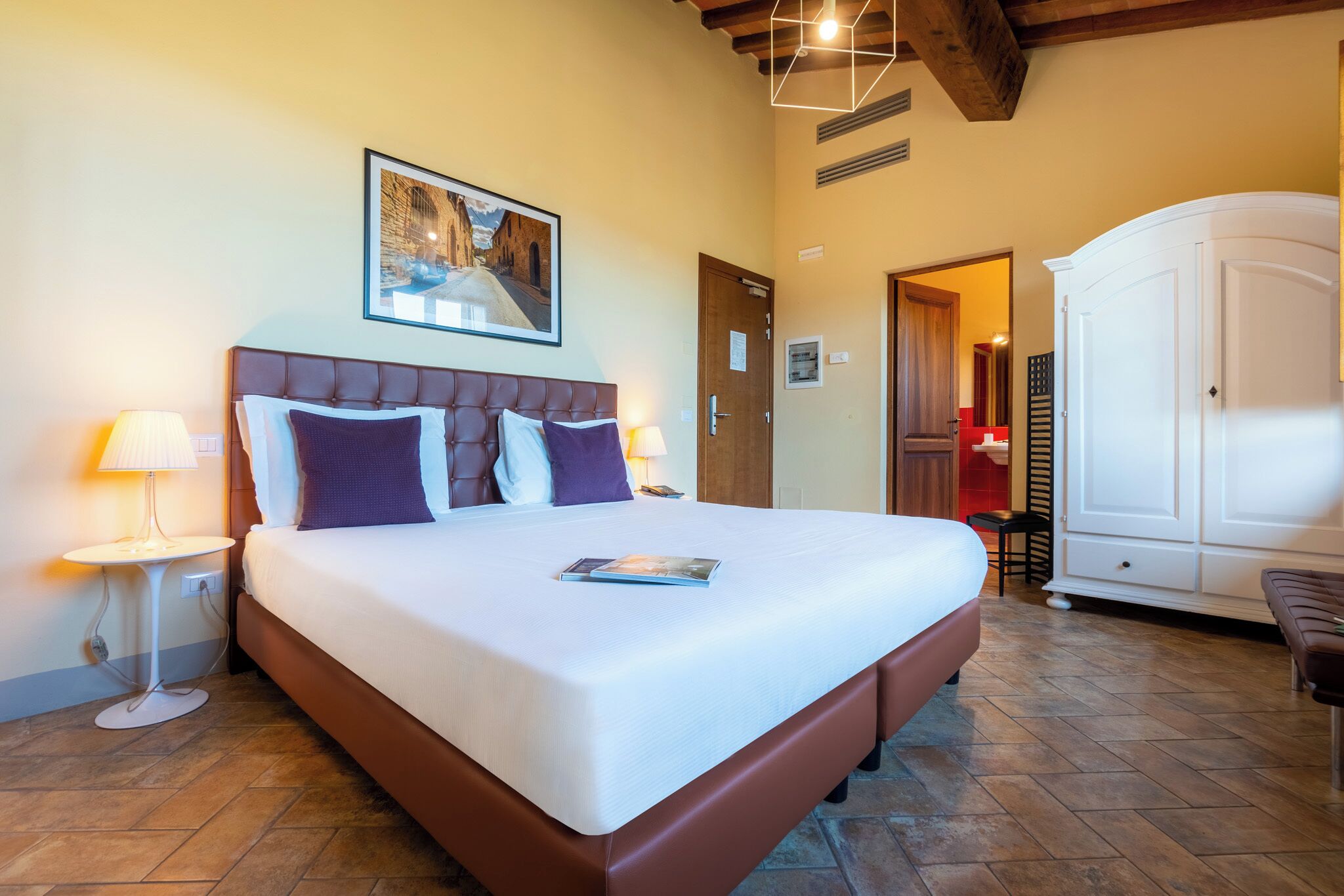 A hotel room with a large bed, a bedside table with a lamp, a wardrobe, and a framed picture on the wall.