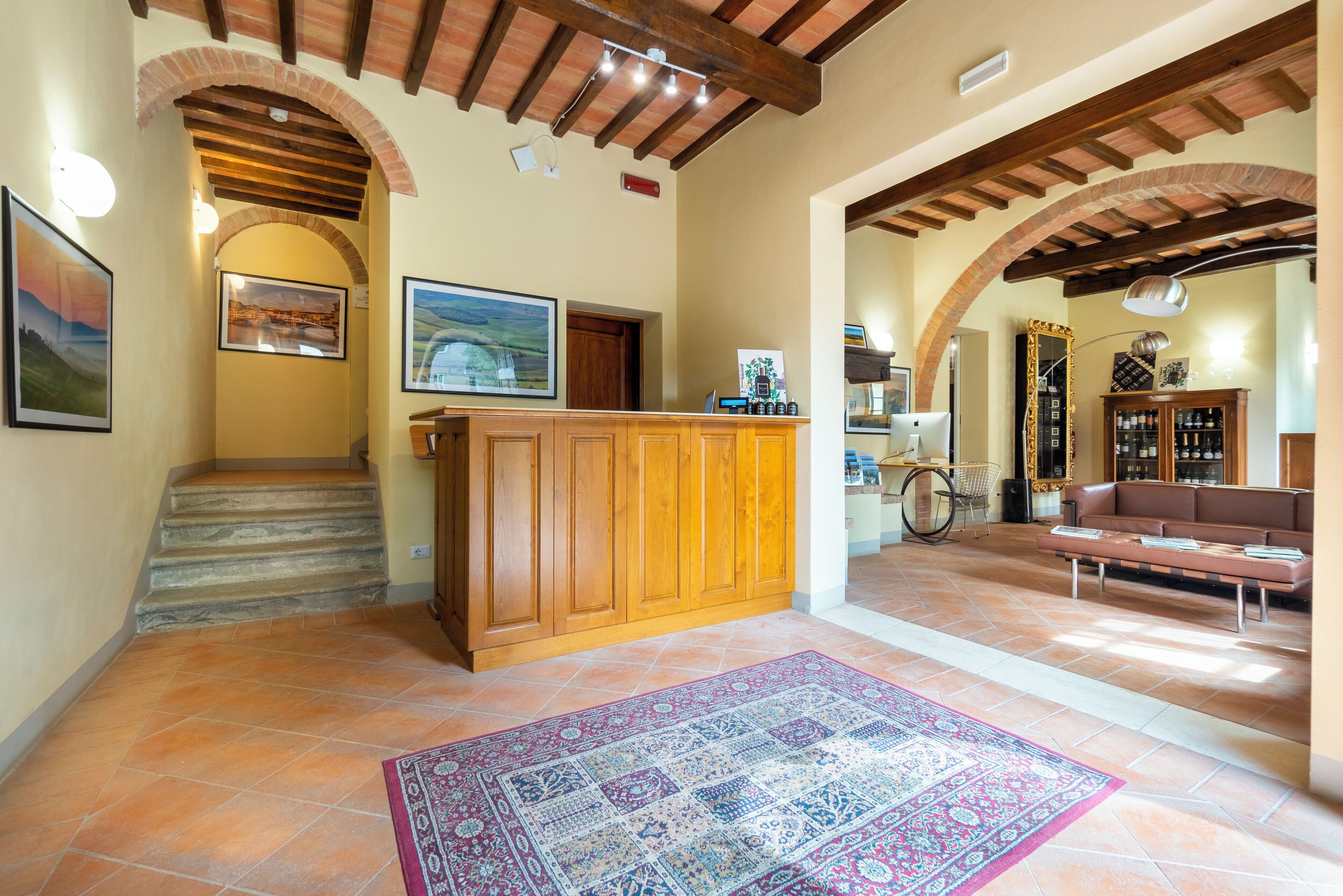 A spacious lobby with a wooden reception desk, a patterned rug, and a staircase leading to upper floors.
