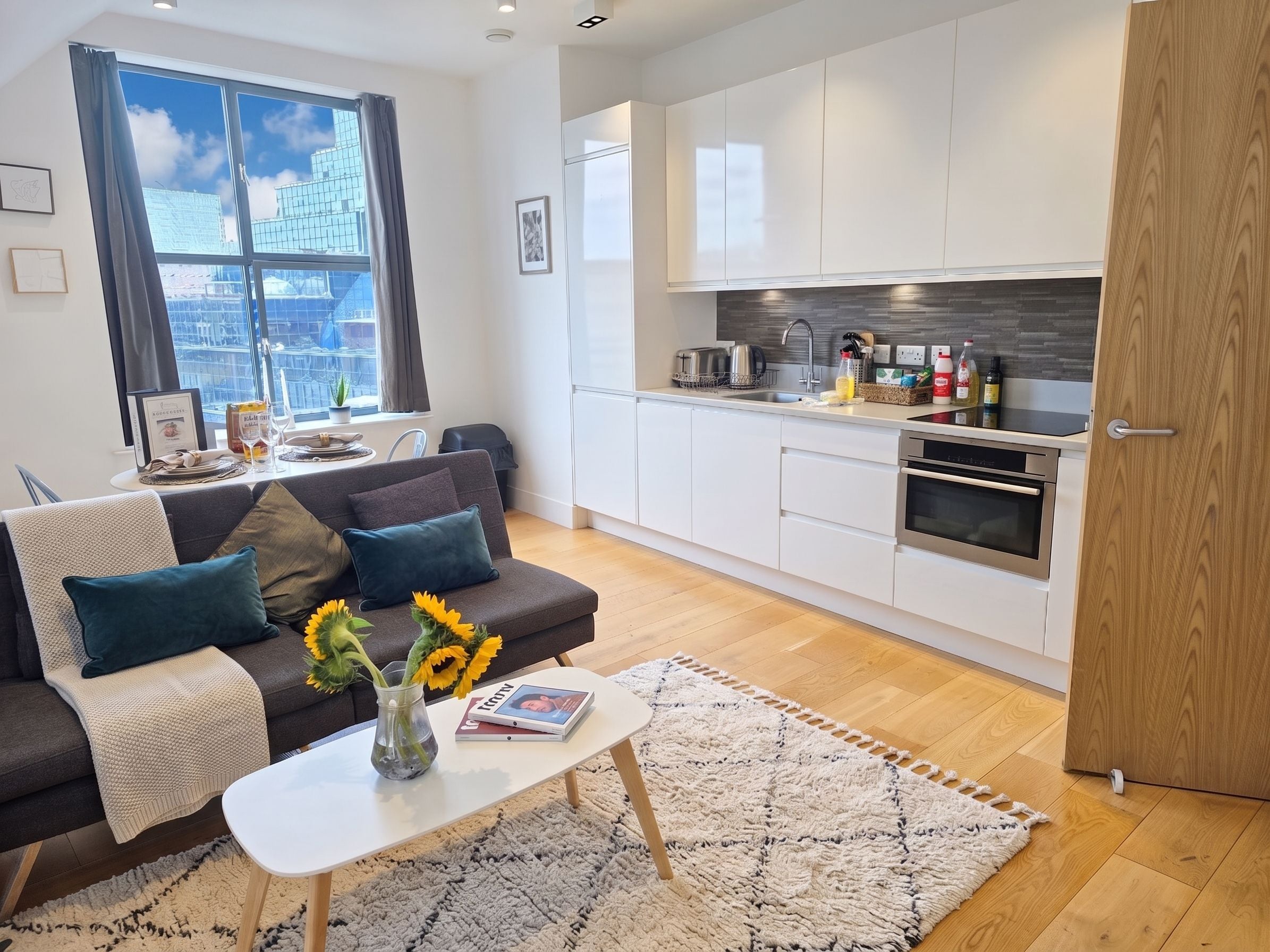 A modern apartment with a living area, kitchenette, and a large window with a city view.