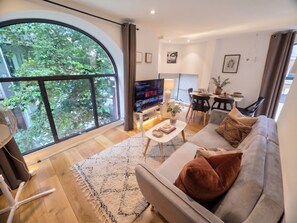 Uma sala de estar moderna com uma janela grande, televisão de tela plana, sofá e área de jantar.