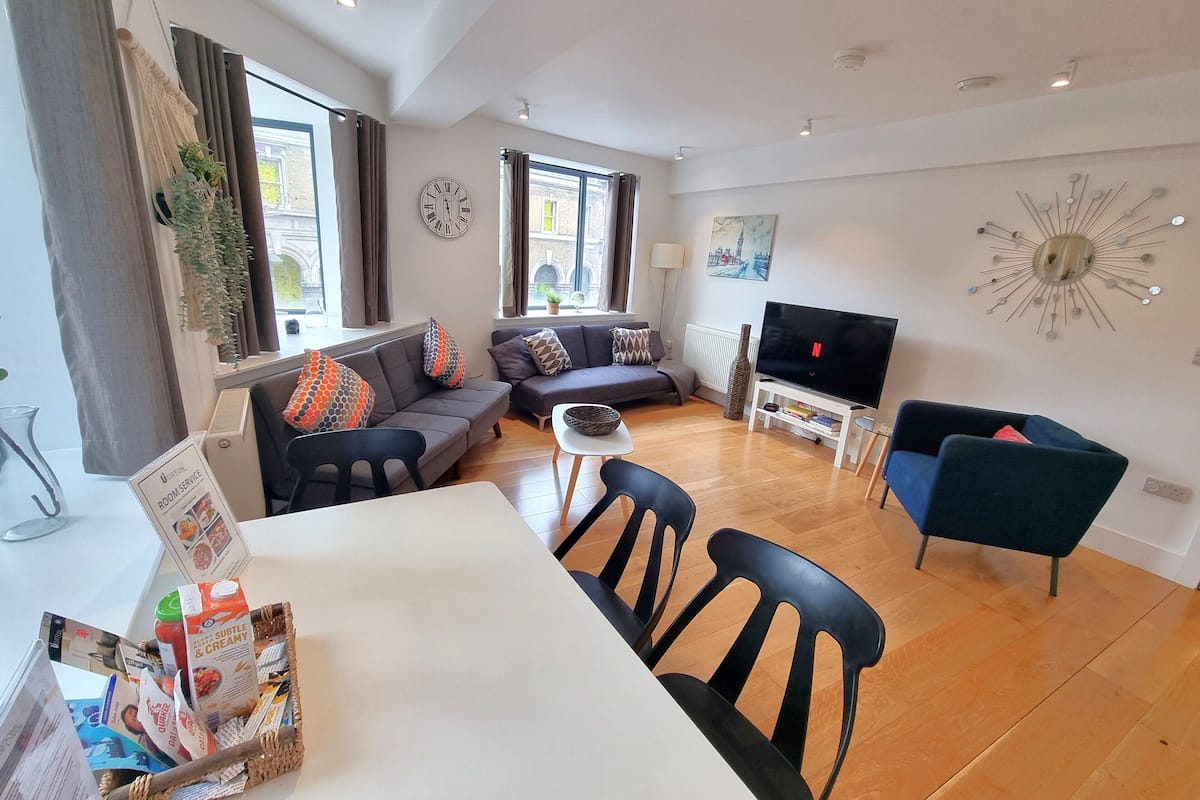 Un salon moderne comprenant un ensemble de canapés, un téléviseur et un coin repas avec des chaises et une table.