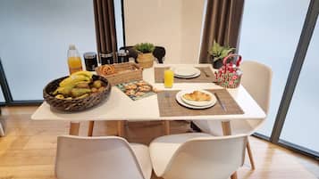 A breakfast table with a fruit bowl, croissant, juice, and a basket of pastries.