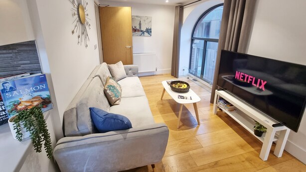 A modern living room with a grey sofa, a coffee table, a flat-screen TV, and a bookshelf. - Urban Stay Shard View Apartments (London)