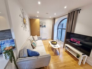 A modern living room with a grey sofa, a coffee table, a flat-screen TV, and a bookshelf. - Urban Stay Shard View Apartments (London)
