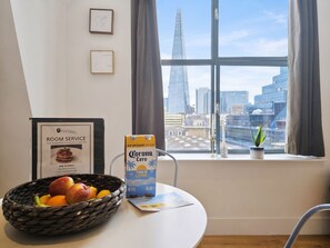 Quarto com vista para o horizonte urbano, um certificado emoldurado na parede, uma cesta de frutas e uma caixa de cerveja Corona sobre a mesa.